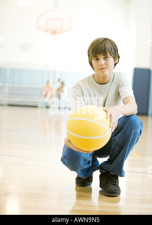 Teen boy crouching with basketball in school gym Stock Photo