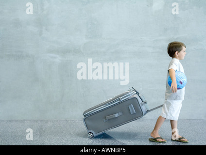 Boy pulling suitcase and carrying globe under arm Stock Photo