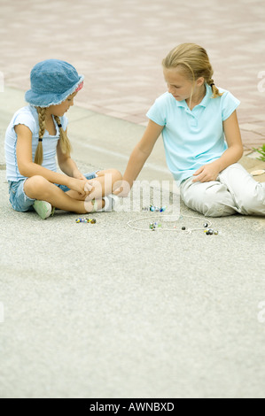 Two girls playing marbles in street Stock Photo