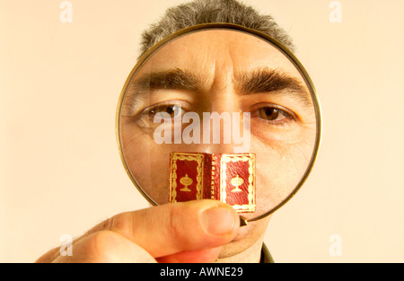 A rare books librarian takes a  close look at a tiny ancient book through a magnifying glass Stock Photo