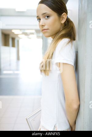 Teen girl leaning against wall, looking at camera