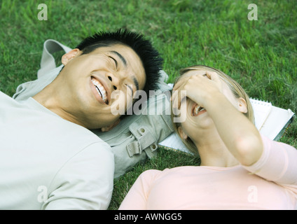 Young couple lying on grass, laughing Stock Photo
