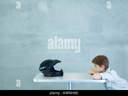 Boy leaning on table, facing helmet Stock Photo