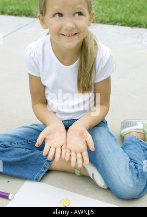 Girl sitting with drawing materials, showing marks on palms Stock Photo