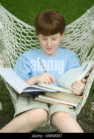Boy sitting in hammock doing homework Stock Photo