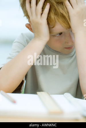 Boy holding head, looking away from homework Stock Photo