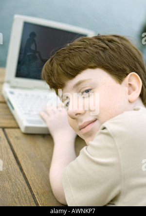 Boy using laptop, looking over shoulder at camera Stock Photo
