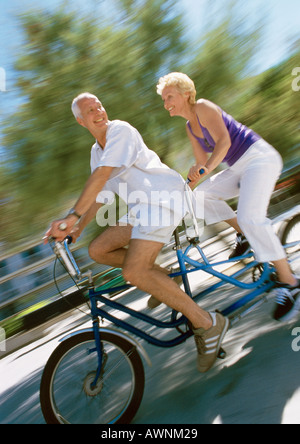 Mature man and woman riding together on tandem bike, side view, blurred Stock Photo