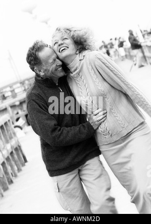 Mature couple walking down boardwalk, laughing, B&W Stock Photo