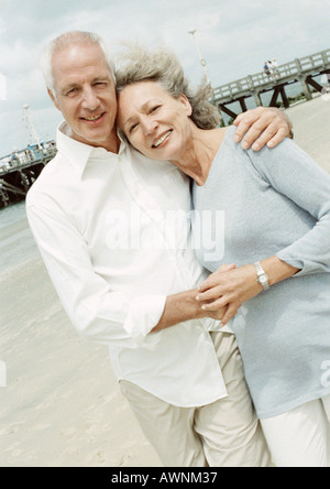 Mature couple with arms around each other on the beach, smiling at camera Stock Photo