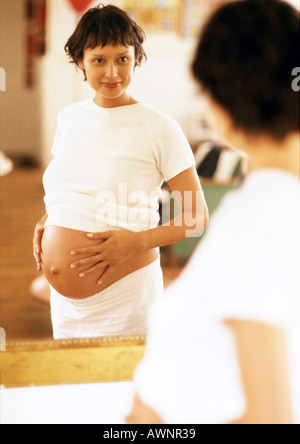 Pregnant woman looking at herself in mirror Stock Photo
