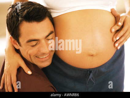 Man pressing cheek to pregnant woman's stomach, close-up Stock Photo
