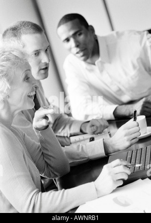 Mature businesswoman in conference, smiling, profile, with two businessmen, B&W Stock Photo