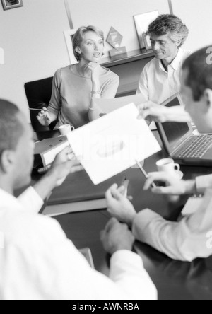 Businesspeople in conference examining document, blurred foreground, B&W Stock Photo