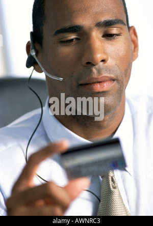 Businessman wearing headset, looking down at credit card in hand, close-up Stock Photo