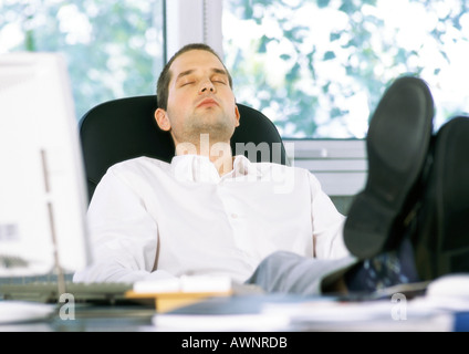 Businessman sitting with feet on desk and eyes closed Stock Photo