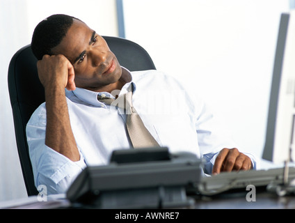 Businessman sitting at desk, head leaning on hand Stock Photo
