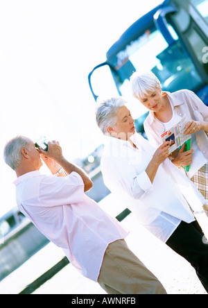 Two mature women looking at map, mature man taking photo Stock Photo