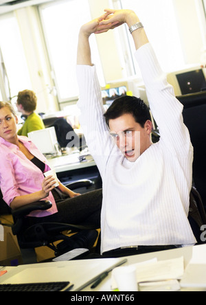 Man stretching in office, colleagues in background Stock Photo