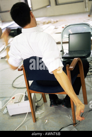 Man sitting in chair stretching arms, in front of laptop computer on chair Stock Photo