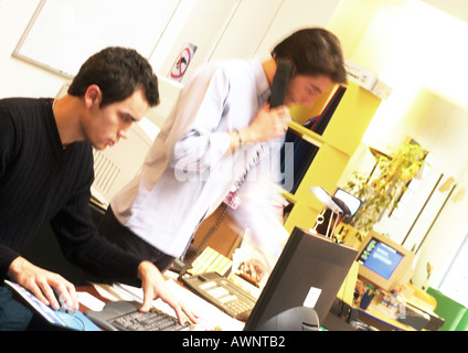 Man working on computer and man standing with telephone Stock Photo