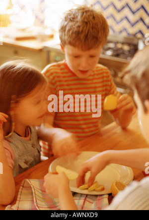Children in kitchen putting apple slices on plate, blurred Stock Photo