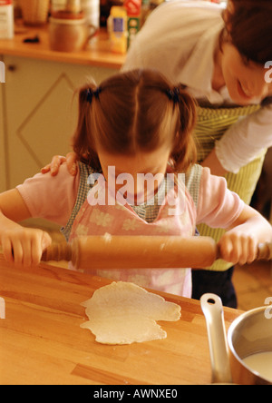 Girl using rolling pin, woman looking over girl's shoulder Stock Photo
