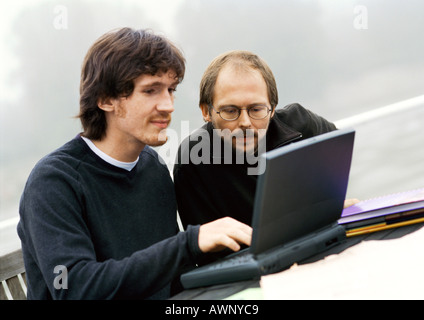 Two men working on laptop computer outdoors Stock Photo