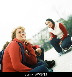 Young people outdoors, one with knee on skateboard Stock Photo