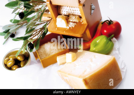 A piece of parmesan cheese with grater, decorated with olive twig, olives, peperonis and tomato Stock Photo