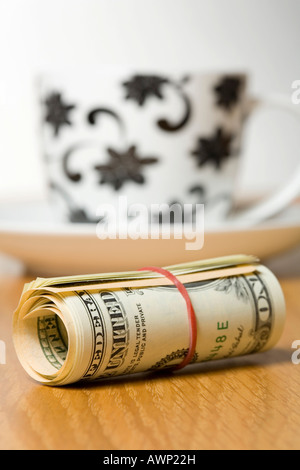 Rolled-up US cash with cup and saucer in background Stock Photo