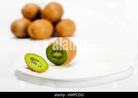 Single kiwi cut open on a plate, more kiwis piled at the back Stock Photo