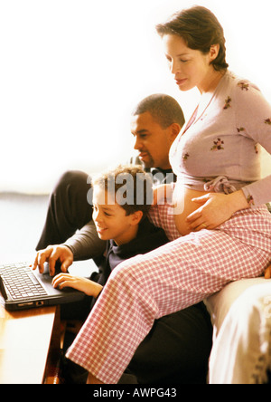Pregnant woman sitting with man and child, child using laptop computer Stock Photo