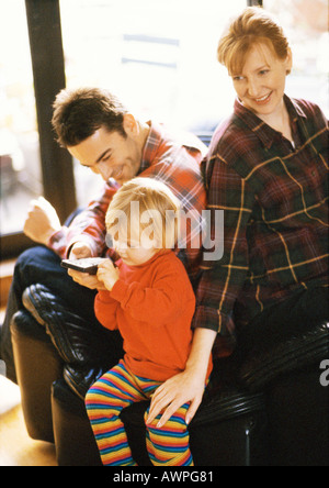 Child sitting in front of parents, holding remote control Stock Photo