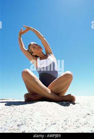 Woman sitting and stretching on the sand. Stock Photo