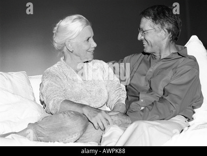 Senior couple holding hands on sofa, smiling at each other Stock Photo