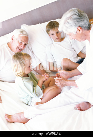 Grandparents and children sitting on bed Stock Photo