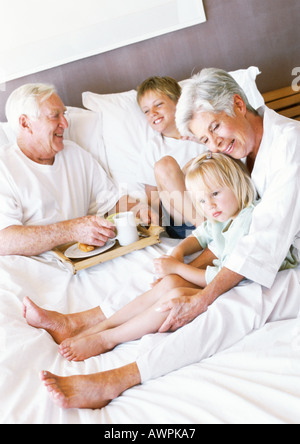 Grandparents and children sitting on bed, man holding breakfast tray Stock Photo