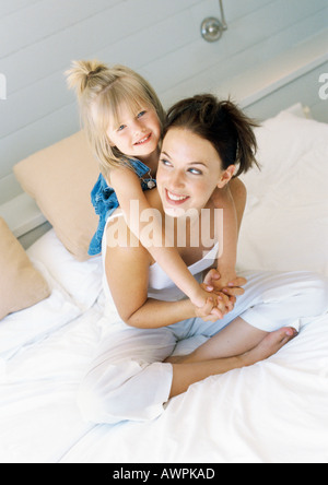 Mother sitting on bed, holding girl on back