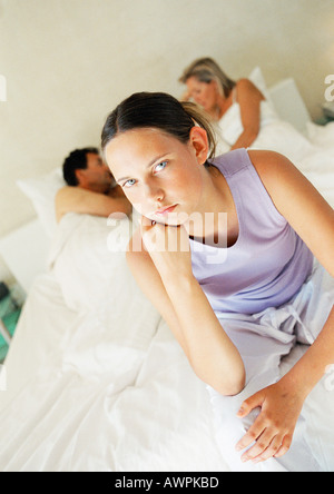 Teenage girl sitting on parent's bed, parents lying in background