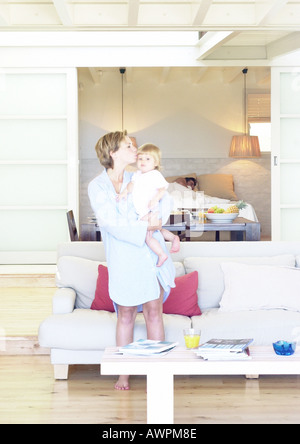 Woman holding baby, man sleeping in background Stock Photo