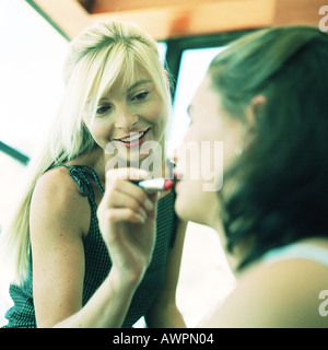 Woman putting lipstick on teenage girl, blurred