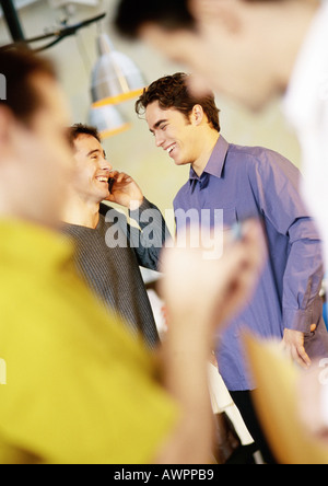 Businessmen standing, one using cell phone Stock Photo