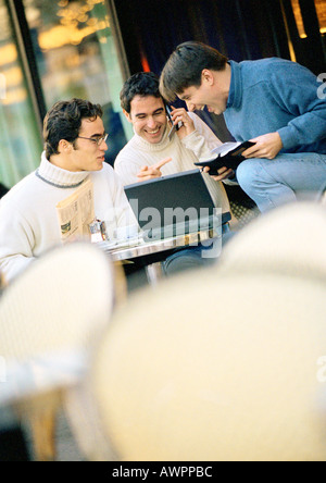 Three men sitting at cafe terrace with laptop computer Stock Photo