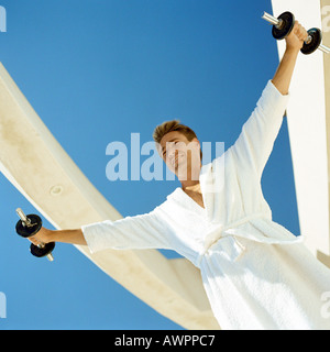 Man lifting weights in bathrobe, low angle view Stock Photo