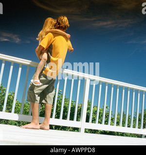 Boy holding little girl next to railing, rear view