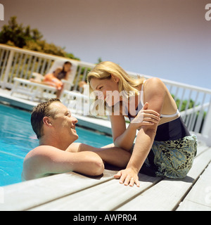 Loving couple at resort, man talking to woman sitting on edge of pool Stock Photo