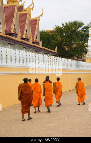 Buddhist monks dressed in orange robes walk along the wall of the Royal Palace, Phnom Penh, Cambodia Stock Photo