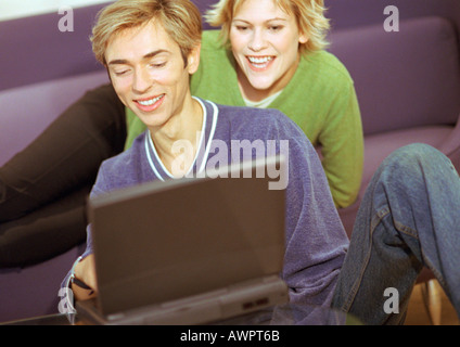Couple smiling, man using laptop, woman sitting, looking over man's shoulder Stock Photo