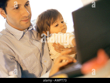 Father and baby, father using laptop, baby sitting on father's lap Stock Photo